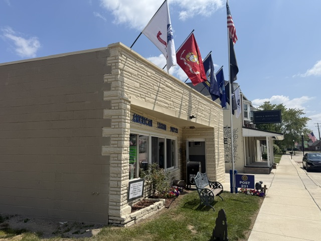 Front of American Legion Post 231 with United States, Marine Corps and other service flags above a memorial bench